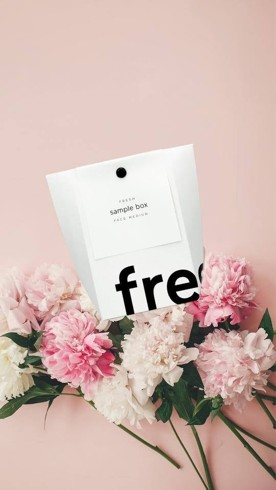 Samplebox von RINGANA auf rosa Hintergrund und wundervollen Blumen gebettet.